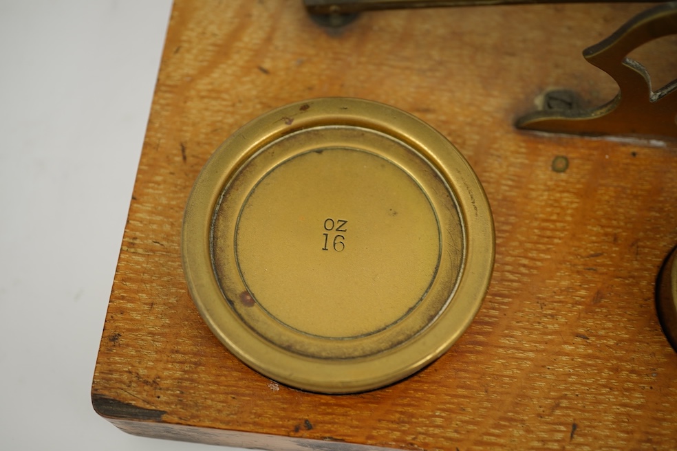 A Sampson Mordan & Co. set of brass postal scales on an oak base with weights, 27cm wide, with engraved prices for Inland Letter Post, etc.